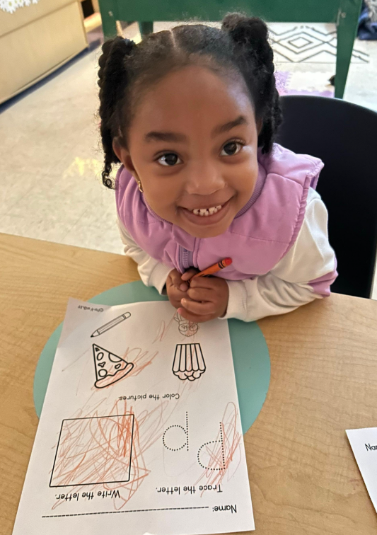 A little girl working on handwritting and smiling to the camera.
