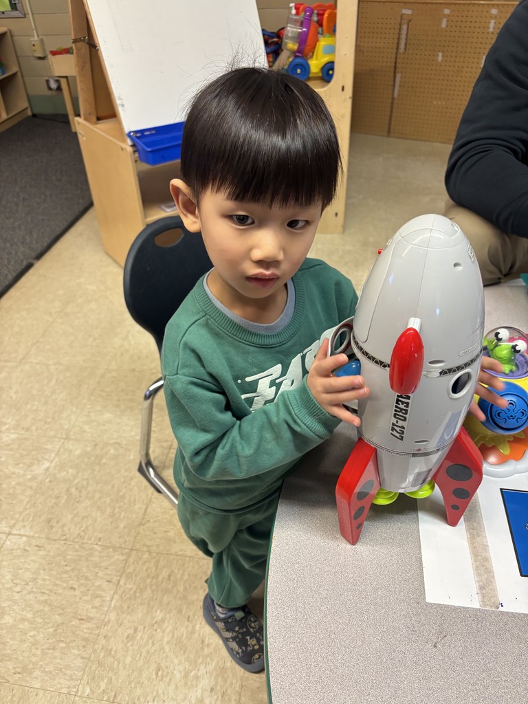A male student sitting at a table and playing with a rocket ship.