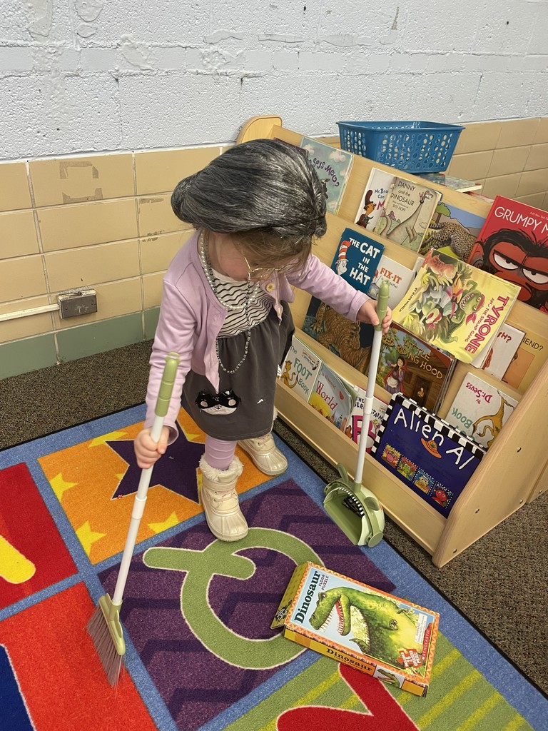 a little girl dressed as a grandma using a dust pan in a classroom