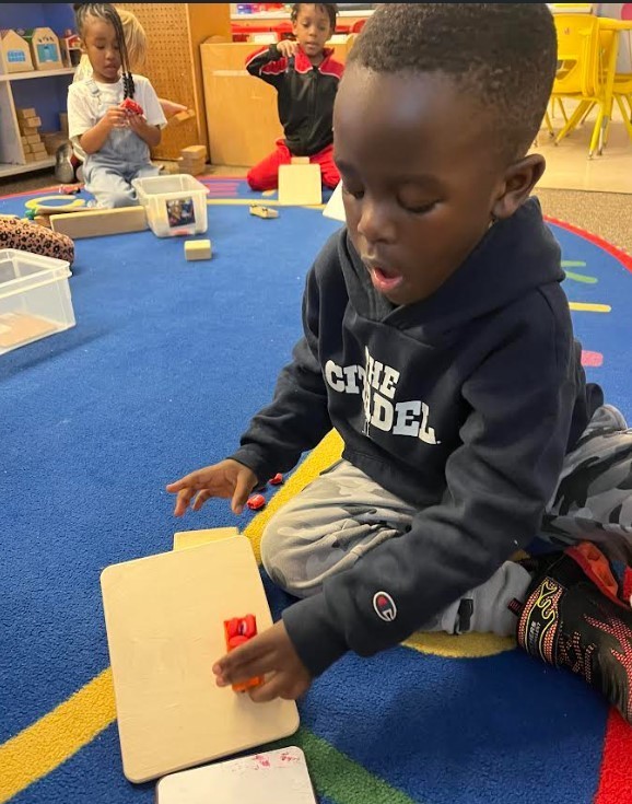 A boy sitting on the floar trying to balance an object.