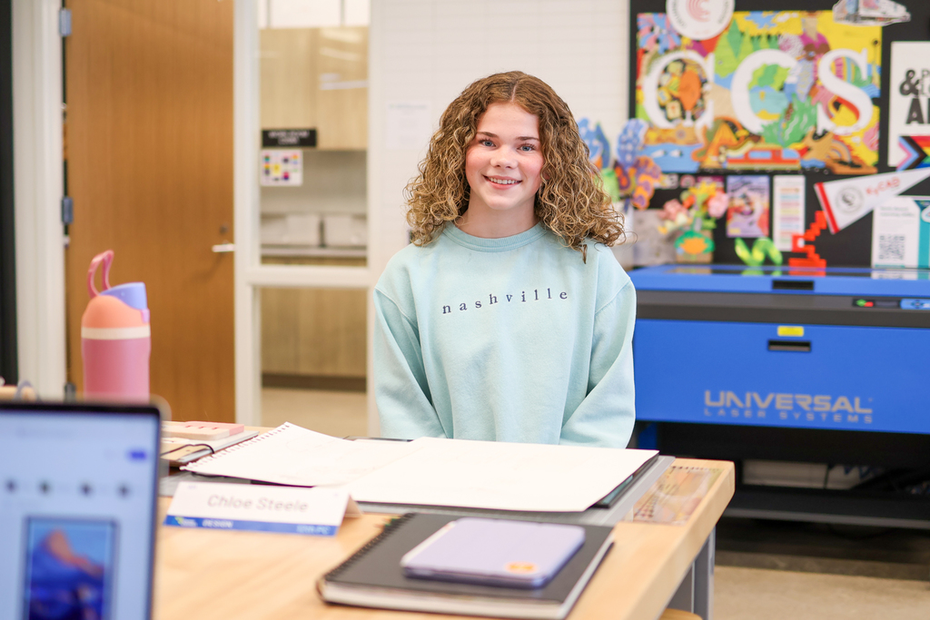 a girl smiling for a photo while sitting at a classroom desk