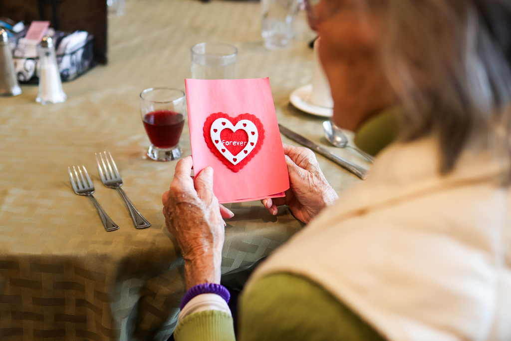 an older woman holding a card with a red heart on it.