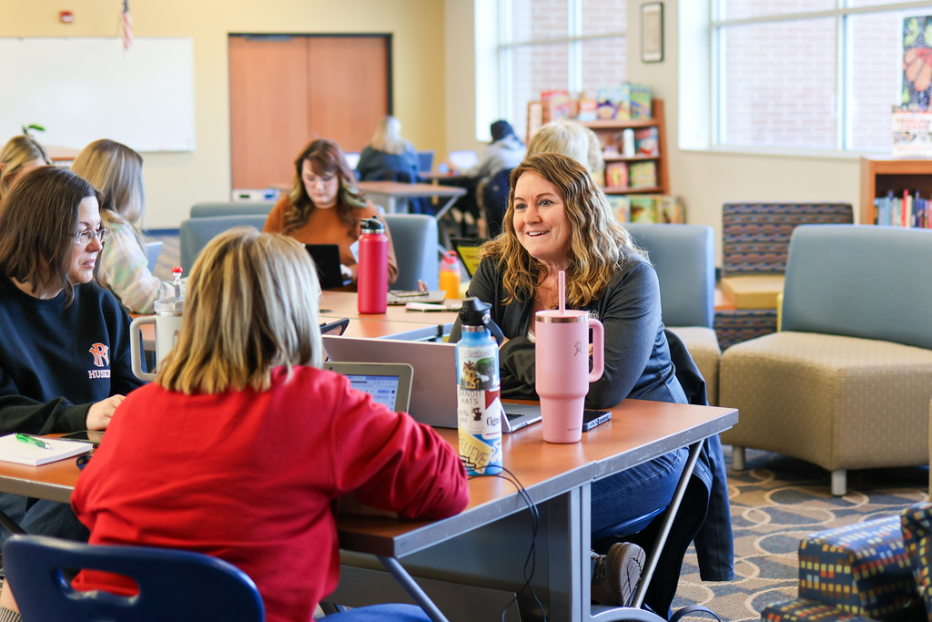 a woman smiling sitting with others at a table in a library 