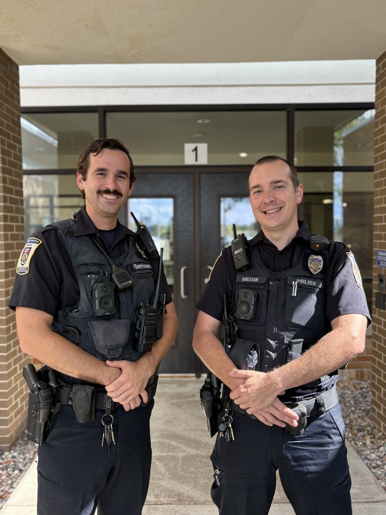 two police officers pose for a photo together in front of a building