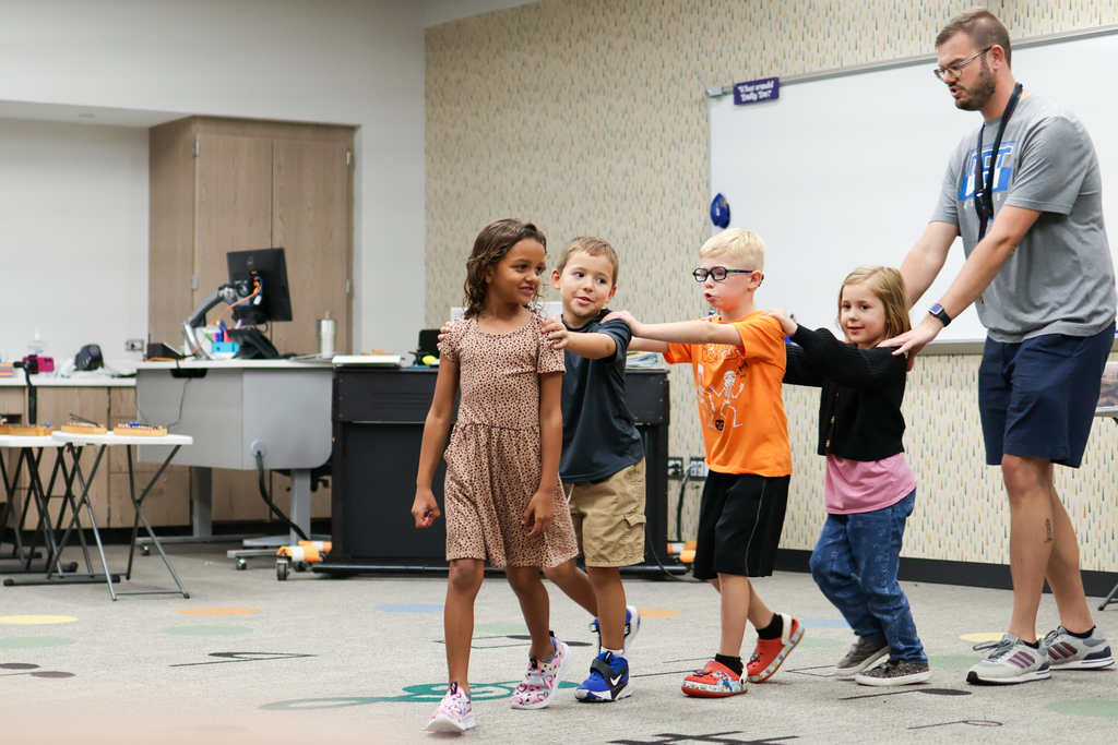a teacher and students walk with hands on shoulders through a school