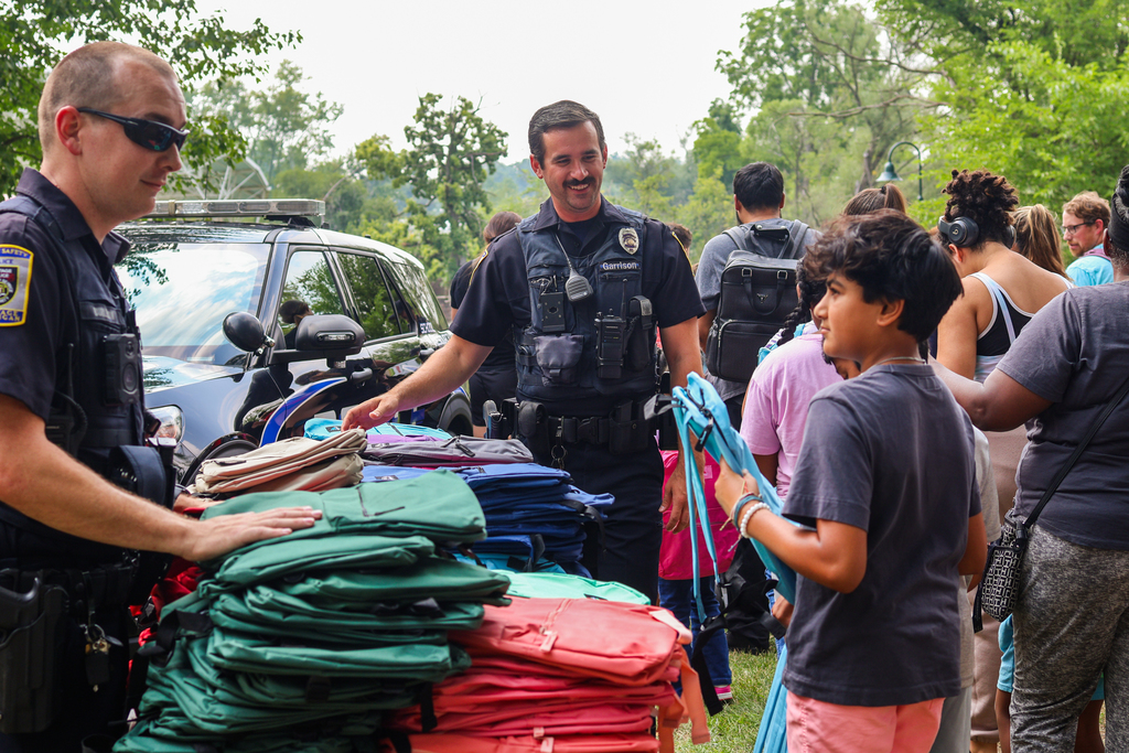 two police officers hand out back packs to students