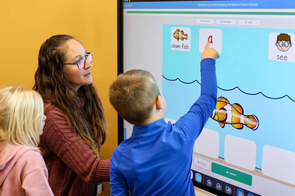 a teacher helping a student choose letters on a touch screen