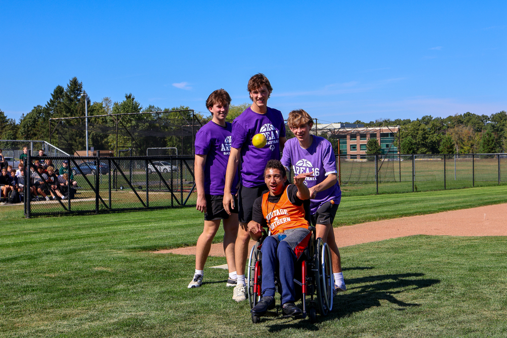 three boys helping another boy in a wheelchair throw a basketball
