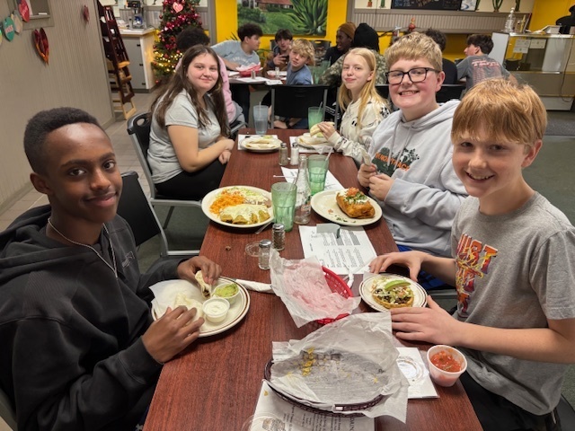 a group of students smile for a photo sitting at a restaurant table