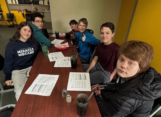 a group of students smile for a photo sitting at a restaurant table