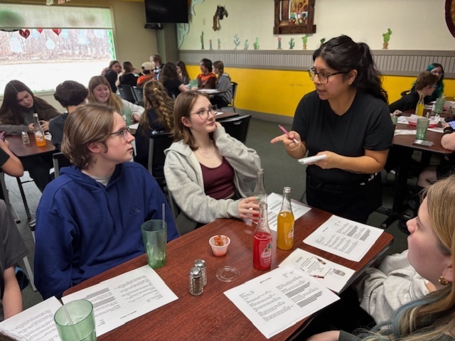 a waitress speaking to students sitting at a table in a restuarant