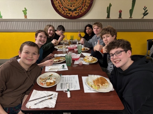 a group of students smile for a photo sitting at a restaurant table