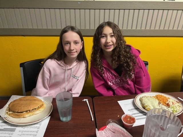 two girls smile for a photo sitting at a restaurant table
