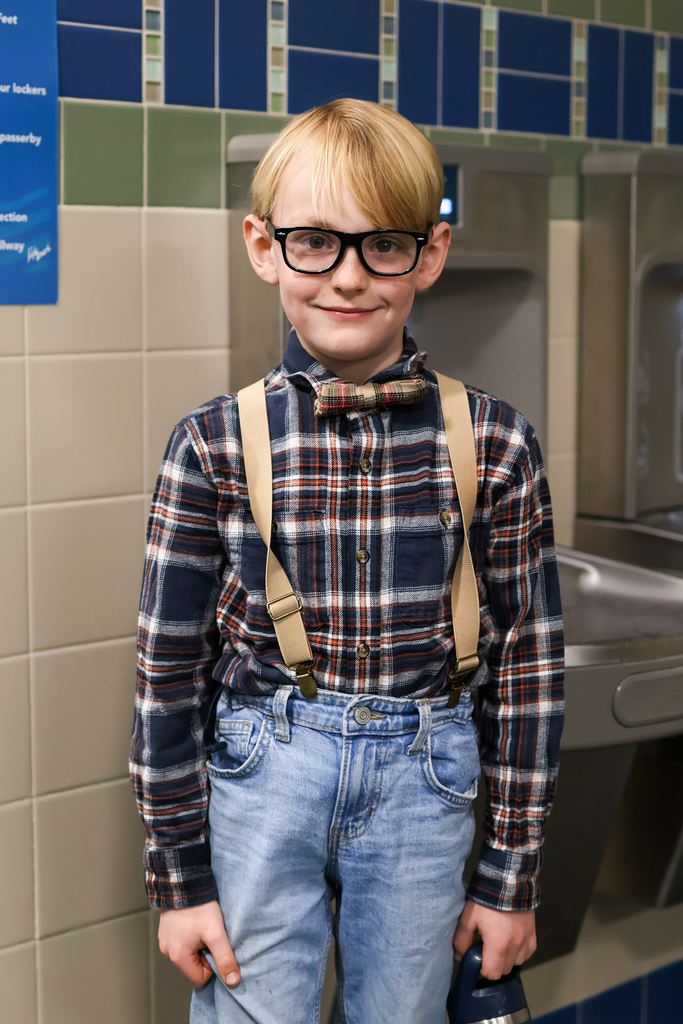 a boy wearing suspenders smiles for a photo in a school hallway