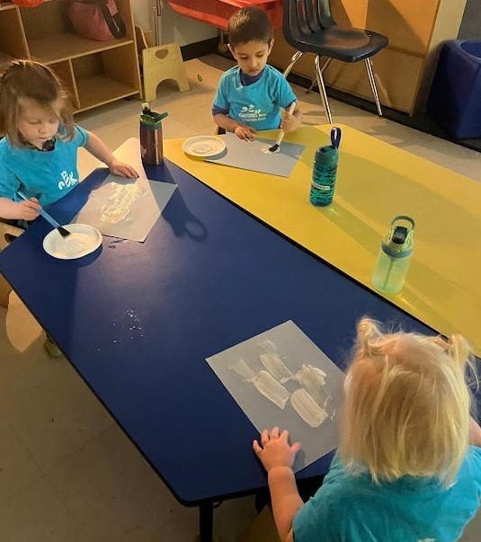 Three students doing a snowman painting at a table.