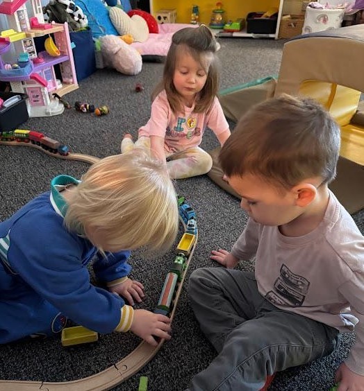 Three toddlers on the floor with a train track.
