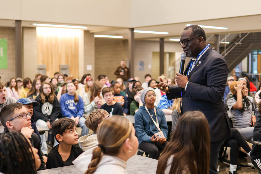 a man speaking to students gathered in a cafeteria
