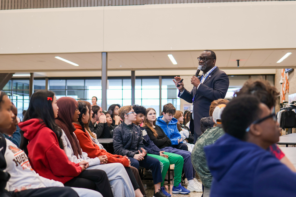 a man speaking to students gathered in a cafeteria