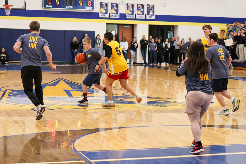 a boy runs with a basketball during a game in a school gym