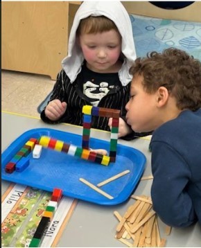 Two boys sitting and looking at small cubes put together.