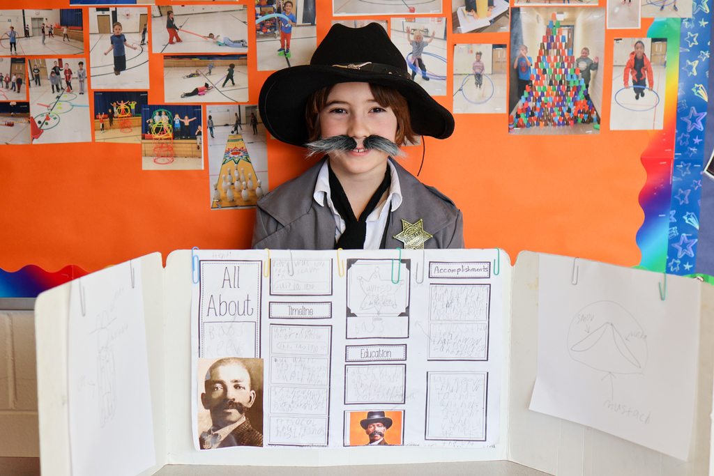 a boy wearing a cowboy hat and fake mustache poses for a photo
