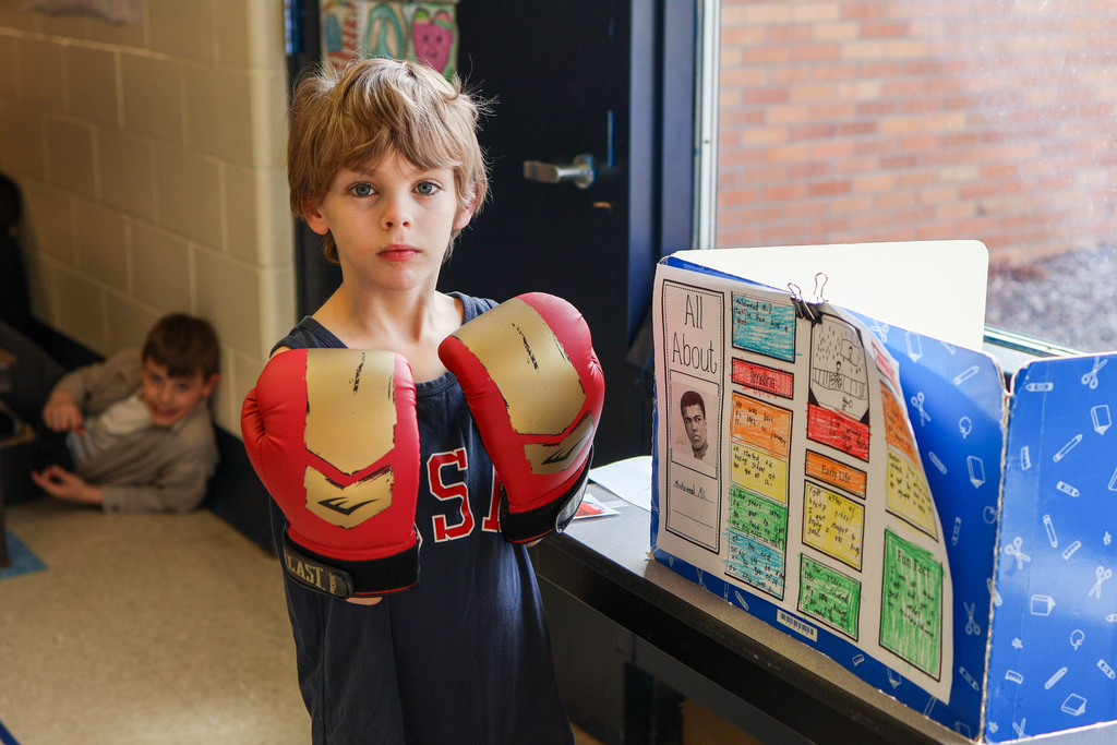 a boy wearing boxing gloves poses for a photo in front of his project