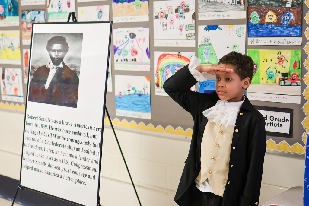 a little boy stands at a military salute next to a poster about the man he's dressed up as
