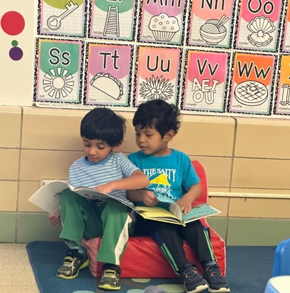 Two boys reading together on a small couch.