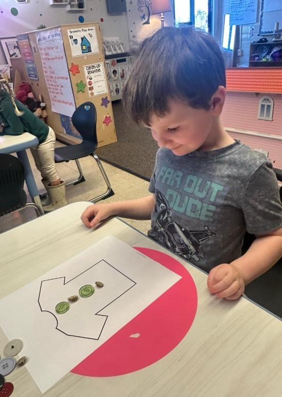 A three year old boy glueing buttons on a shirt.