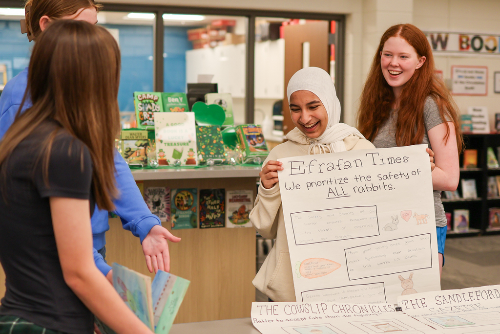 students holding a presentation board laughing in a school library