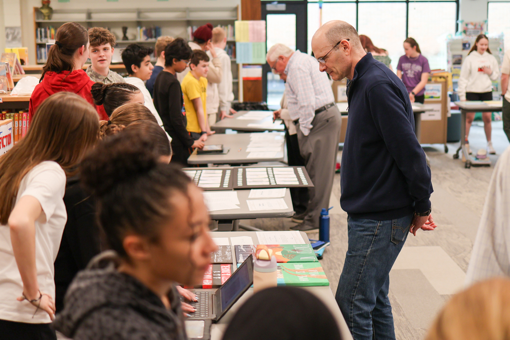 students line one side of tables while adults look at projects on the other side