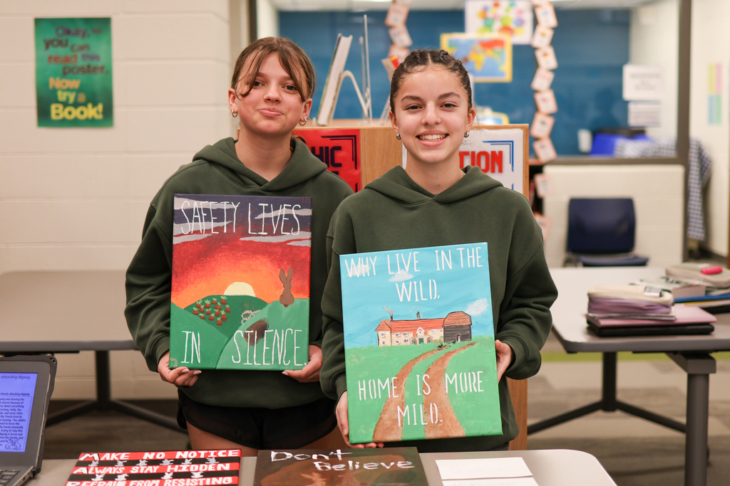 two students smile for a photo holding their paintings