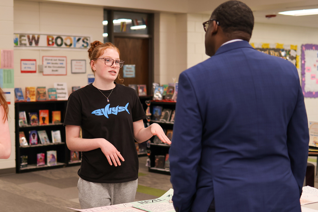 a girl speaking to a man in a school library