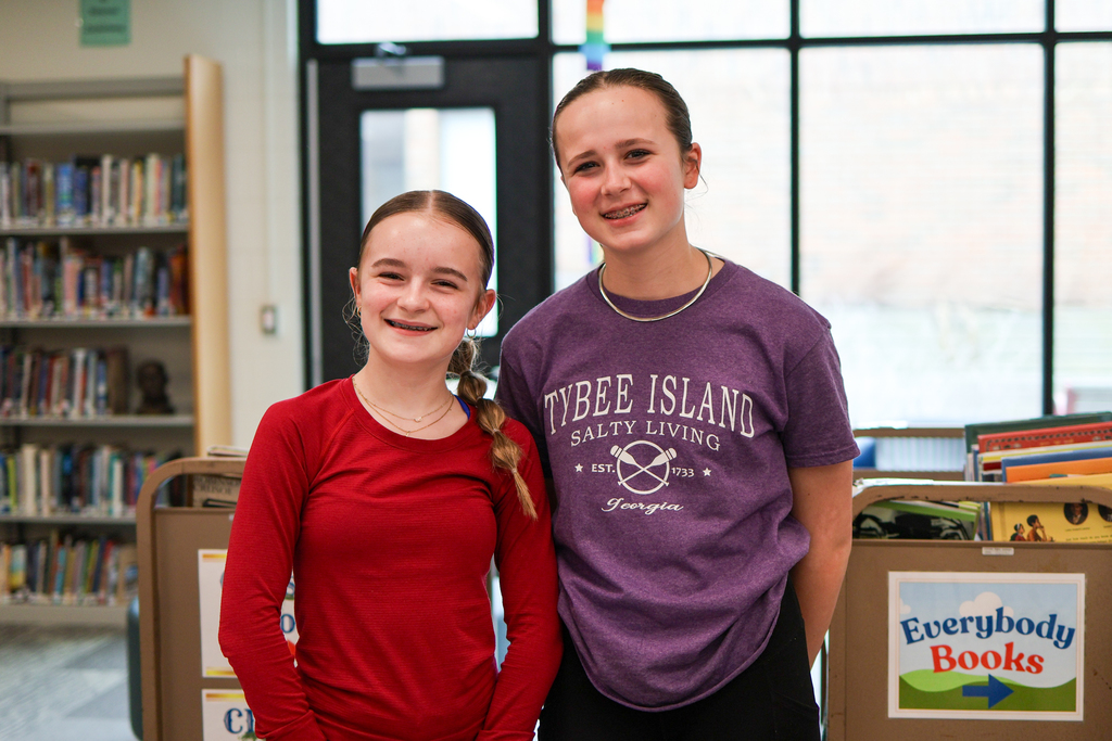 two girls pose for a photo in a library