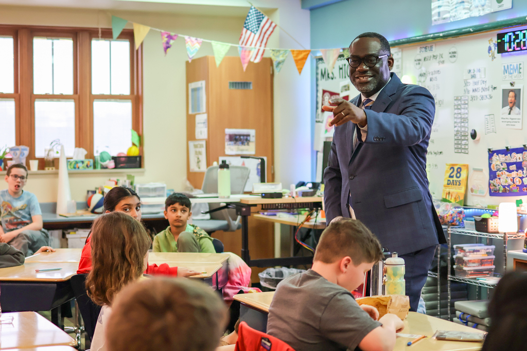 a man points at students and smiles standing at the front of a classroom