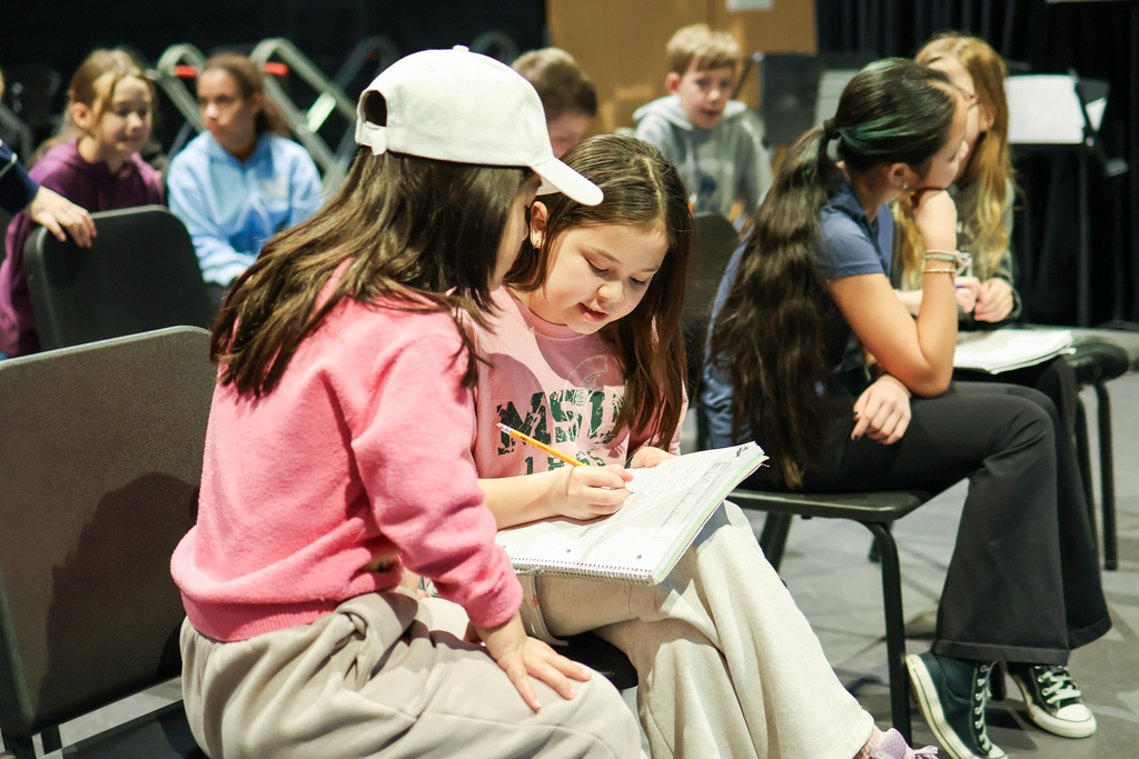 two girls writing in a notebook together in a classroom