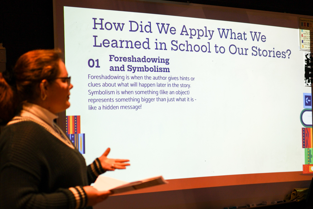 a screen that reads "how did we apply what we learned in school to our stories?" seen behind a woman speaking
