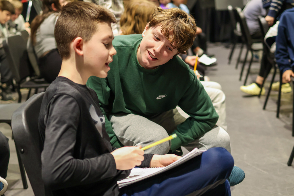 two boys writing in a notebook sitting together in a classroom