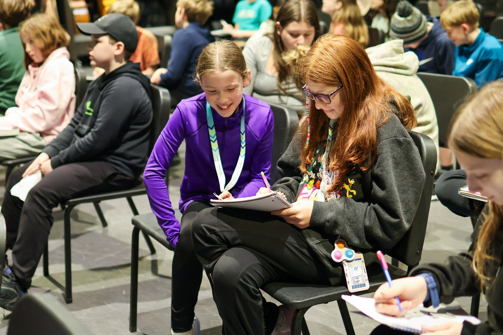 two girls writing in a notebook together in a classroom