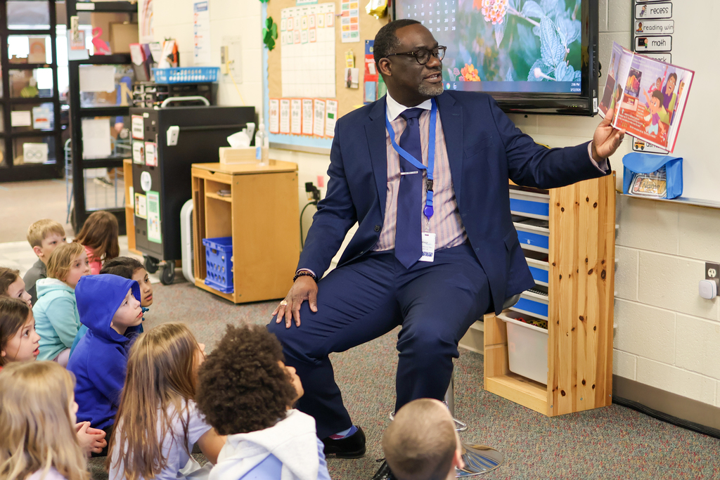 a man reading a book to students in a classroom