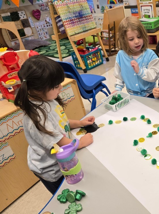 Two students making a patter trail with rocks at a table.