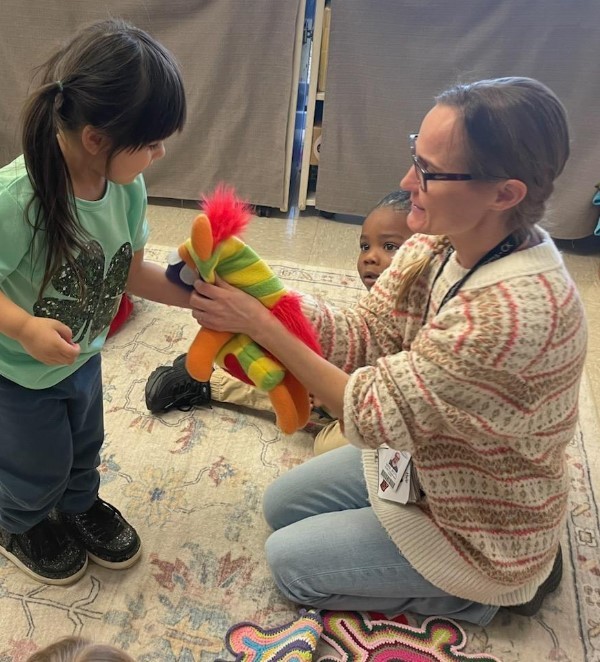 Teacher and a little girl playing with a colorful puppet.