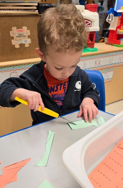 A boy working on cutting with adaptive scissors. 