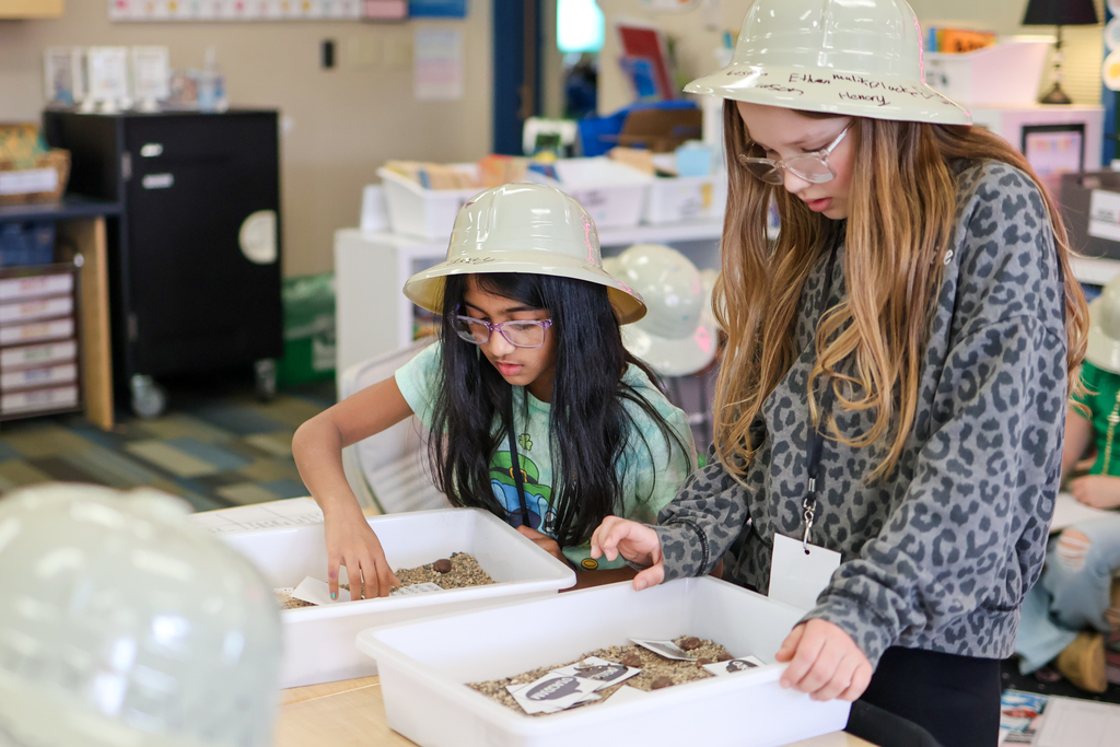 two girls digging through sand in a classroom