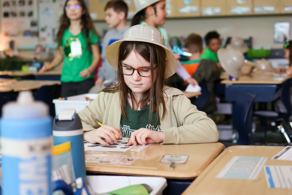 a girl wearing a hat sitting at a desk in a classroom
