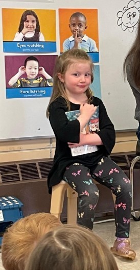 A little girl helping her Mom read a book to the class.