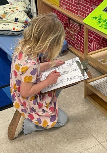 A little girl on her knees looking at a clipboard.