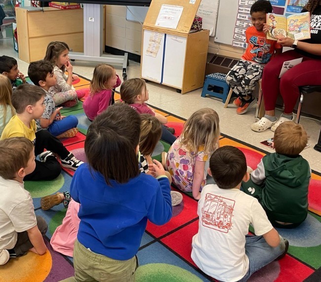 Students sitting together at a colorful rug. 
