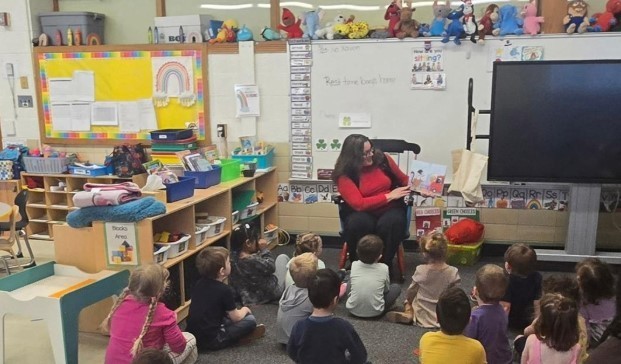 A parent reading a book to a class of students on the rug.