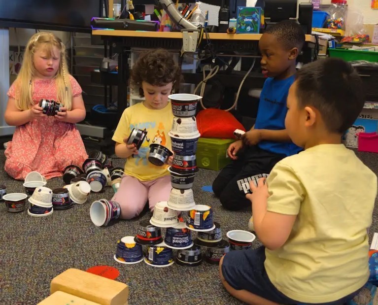 Two girls and two boys stacking recylced yogurt cups.